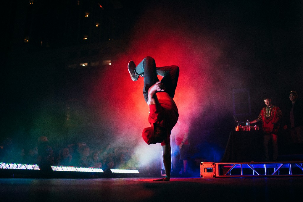 Breakdancer performing dynamic spin under red stage spotlights